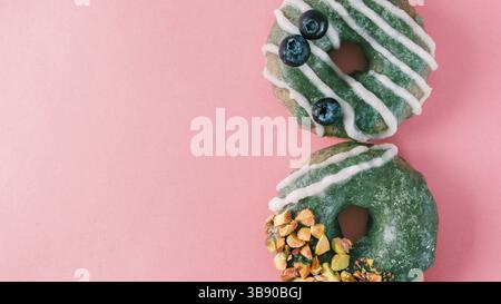 Vegan doughnuts with chia seeds topped with healthy spirulina glaze with pistachio and blueberry. Blue green spirulina donuts on pink background. Copy Stock Photo