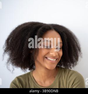 Smiling dark-skinned woman with natural curly hair looking down, perfect for beauty, diversity, positivity, lifestyle and self-confidence themes. Stock Photo