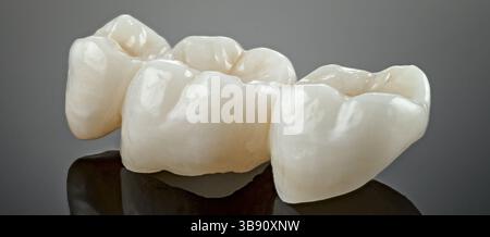 Metal free ceramic dental crowns. Imitation of a dental prosthesis of a dental bridge for three teeth on a grey background. Close-up Stock Photo