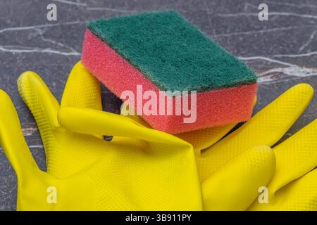 yellow household rubber gloves with red scouring sponge on a marble background. Household concept. Stock Photo