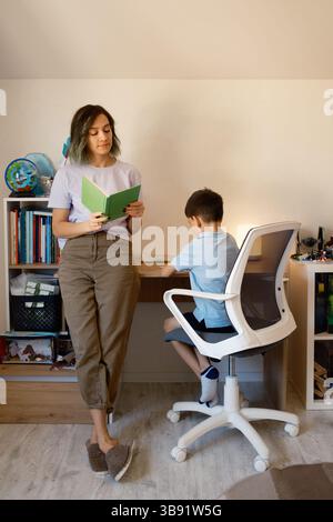 Mother assisting son with homework in cozy home study space Stock Photo