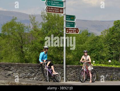 Two young female tourists with bicycles at rural crossroad and multiple road signs in Killorglin Ireland exploring the Irish countryside on vacation Stock Photo