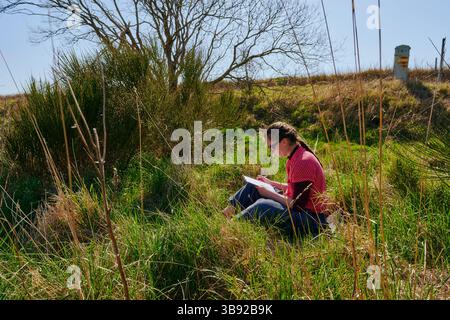 A caucasian woman enjoys some contemplative 'me time' alone with her notebook in a quiet sunny countryside spot. Stock Photo
