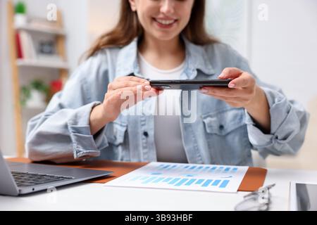 Woman taking photo of document using scanning app on smartphone at desk in office, closeup Stock Photo