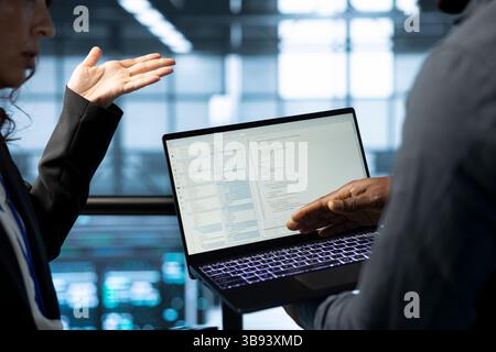 Software developers using laptop in data center, managing server virtualization. IT expert coding on notebook in server room, finetuning network protocols, enforcing advanced security measures Stock Photo
