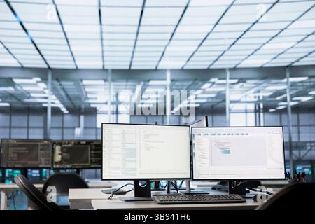 Code running on computer displays in empty data center workspace, used for troubleshooting rackmounts. Binary script running on desktop PC monitors upgrading mainframes systems in server room Stock Photo