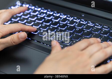 Hands Typing on Backlit Keyboard of Modern Laptop in Close-Up View. Stock Photo
