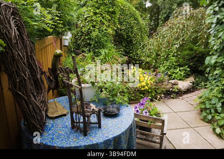 Rustic Vitis - Vines wreath and wooden miniature chair on round table draped with a blue, green and orange flowery tablecloth, yellow Oenothera etc. Stock Photo