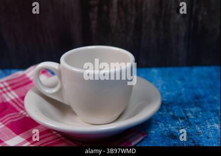 A white ceramic cup and saucer on blue with a red and white linen napkin. Stock Photo