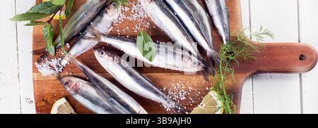 Fresh sprat fish with herbs and lemon on a white wooden background. Top view. Panorama. Stock Photo