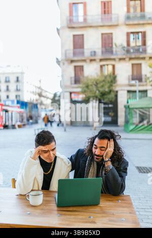 Gay couple using laptop and having problems at outdoor cafe Stock Photo