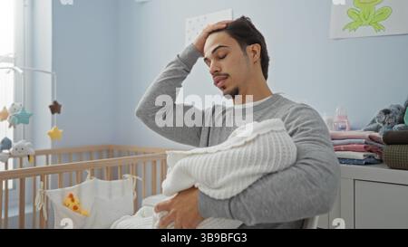Young man in bedroom holding baby wrapped in blanket looking thoughtful in bright nursery with crib and playful decorations suggesting family love and Stock Photo
