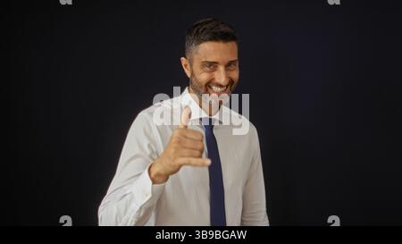 Hispanic man makes a surfer hand gesture while smiling against a black background, exuding confidence and charm in a portrait setting. Stock Photo