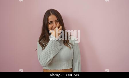 Woman smiling with hand covering face stands against pink background radiating beauty and charm. Stock Photo