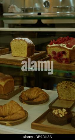 Assorted pastries including loaf cake and croissants displayed on wooden trays in a cozy restaurant setting showcasing delicious baked goods indoors. Stock Photo