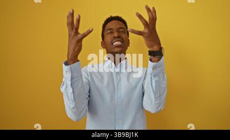 Young african american man expressing frustration with raised hands against isolated yellow background. Stock Photo