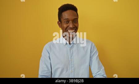 Smiling young african american man in casual shirt poses in front of vibrant yellow background exuding confidence and charm while making eye contact w Stock Photo