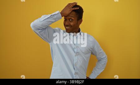 Young man with surprised expression holds his head with hand on isolated yellow background, showcasing emotion and style Stock Photo
