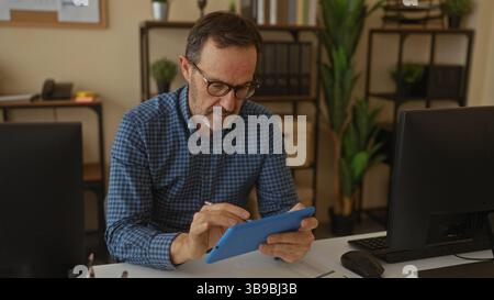 Mature man in glasses focusing on a tablet in a well-organized office with various plants creating a thoughtful modern workplace atmosphere. Stock Photo