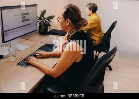 Professionals seated at desks working on computers in an office, emphasizing focus and productivity in a modern work environment with a collaborative Stock Photo