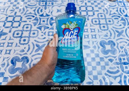 Hand Holding a Bottle of ACE Pavimenti Floor Cleaner on a Blue and White Patterned Surface Stock Photo