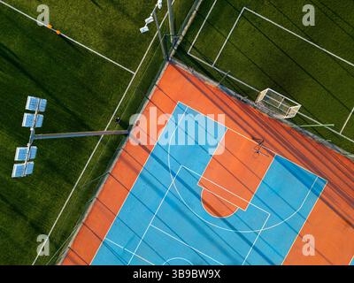 Outdoor basketball and soccer court at sunset with colorful surface, long shadows, and green artificial turf in the background Stock Photo