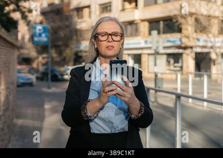 A confident business woman is seen in an urban environment using her smartphone effectively Stock Photo