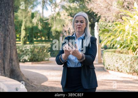 Businesswoman using smartphone in a park during a sunny day Stock Photo