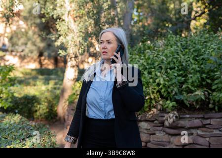 A professional woman engaged in a phone conversation while surrounded by an outdoor setting Stock Photo