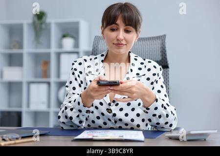 Woman taking photo of document using scanning app on smartphone at desk in office Stock Photo