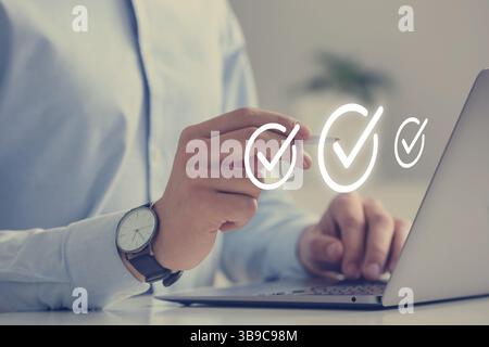 Approved. Man using laptop and touching virtual screen with check marks at table, closeup Stock Photo