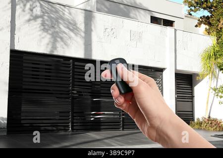 Woman using remote to control roller shutters outdoors, closeup Stock Photo