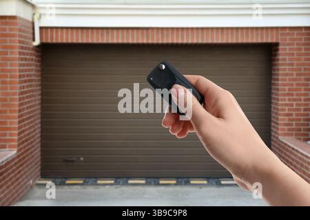 Woman using remote to control garage door outdoors, closeup Stock Photo