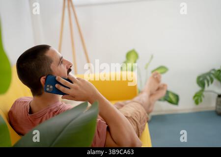 Relaxed man is casually talking on the phone while seated in his cozy living room space Stock Photo