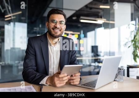 Portrait of a successful young businessman, the man is smiling and looking at the camera. The company employee in a business suit is holding a tablet computer and a laptop in his hands. Stock Photo