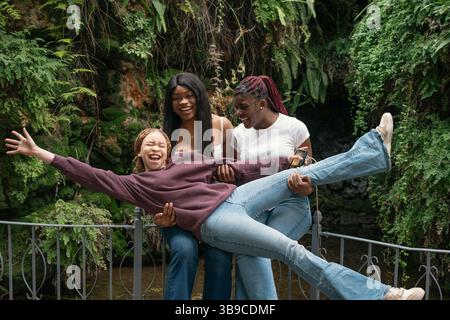 Three young women having fun in a park lifting their friend Stock Photo