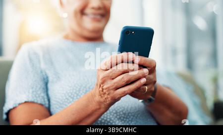 Senior woman, hands and typing with phone for game, word search or online entertainment on sofa at home. Closeup, elderly or female person with smile Stock Photo