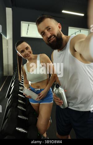 Couple with water bottles taking selfie after training in gym Stock Photo