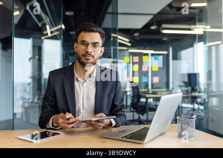 A young programmer in a suit smiles while working in a modern office environment, ready for business and efficiency Stock Photo