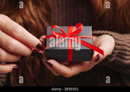 Woman opening gift box. Hands untying red ribbon. Present in female hands. Surprise moment. Holiday celebration concept. Christmas or birthday gift. Stock Photo
