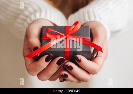 Small gift box in hands. Present with red ribbon. Holiday surprise. Closeup of female hands. Festive moment celebration concept. Giving and sharing. Stock Photo