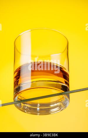 A classic whiskey glass filled with golden amber whiskey, yellow background Stock Photo
