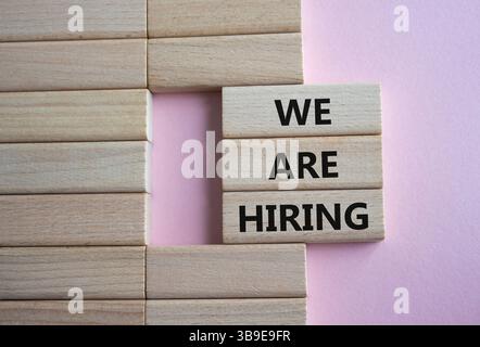 We are Hiring symbol. Concept words We are Hiring on wooden blocks. Beautiful pink background. Business and We are Hiring concept. Copy space. Stock Photo