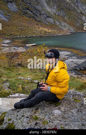 Man in yellow jacket flying fpv drone wearing goggles in a fjord of Norway. Stock Photo