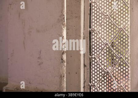 Close up of a weathered white wall next to a perforated metal sheet Stock Photo