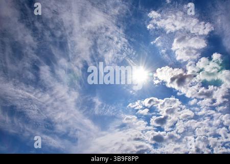 Bright sun between cirrus and cumulus clouds Stock Photo