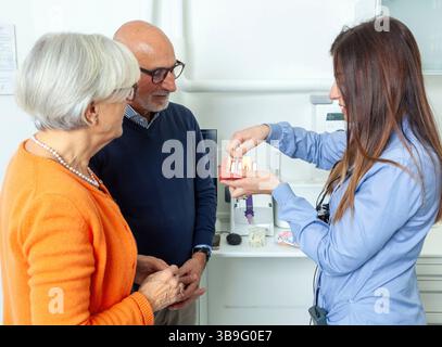 Dentist explaining dental implant procedure to senior couple using a denture model in dental clinic Stock Photo