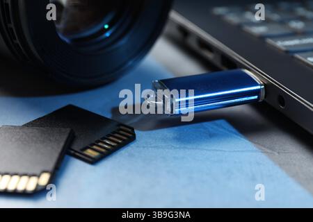 Flash drive connected to laptop, SD memory cards and camera lens on gray table, closeup Stock Photo