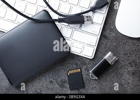 SD memory card, USB flash drive, hard disk drive with cable and keyboard on dark grey table, flat lay Stock Photo