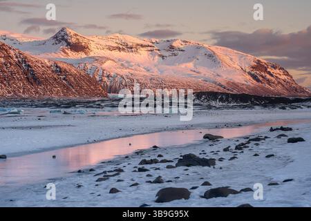 Majestic Icelandic landscape with sunset hues on snow-covered peaks, reflected in icy waters. A stunning display of nature in Iceland's winter wonderl Stock Photo